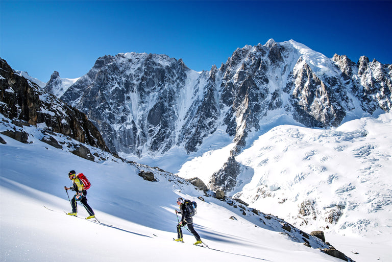 two backcountry skiers skinning uphill with large mountain peak in background